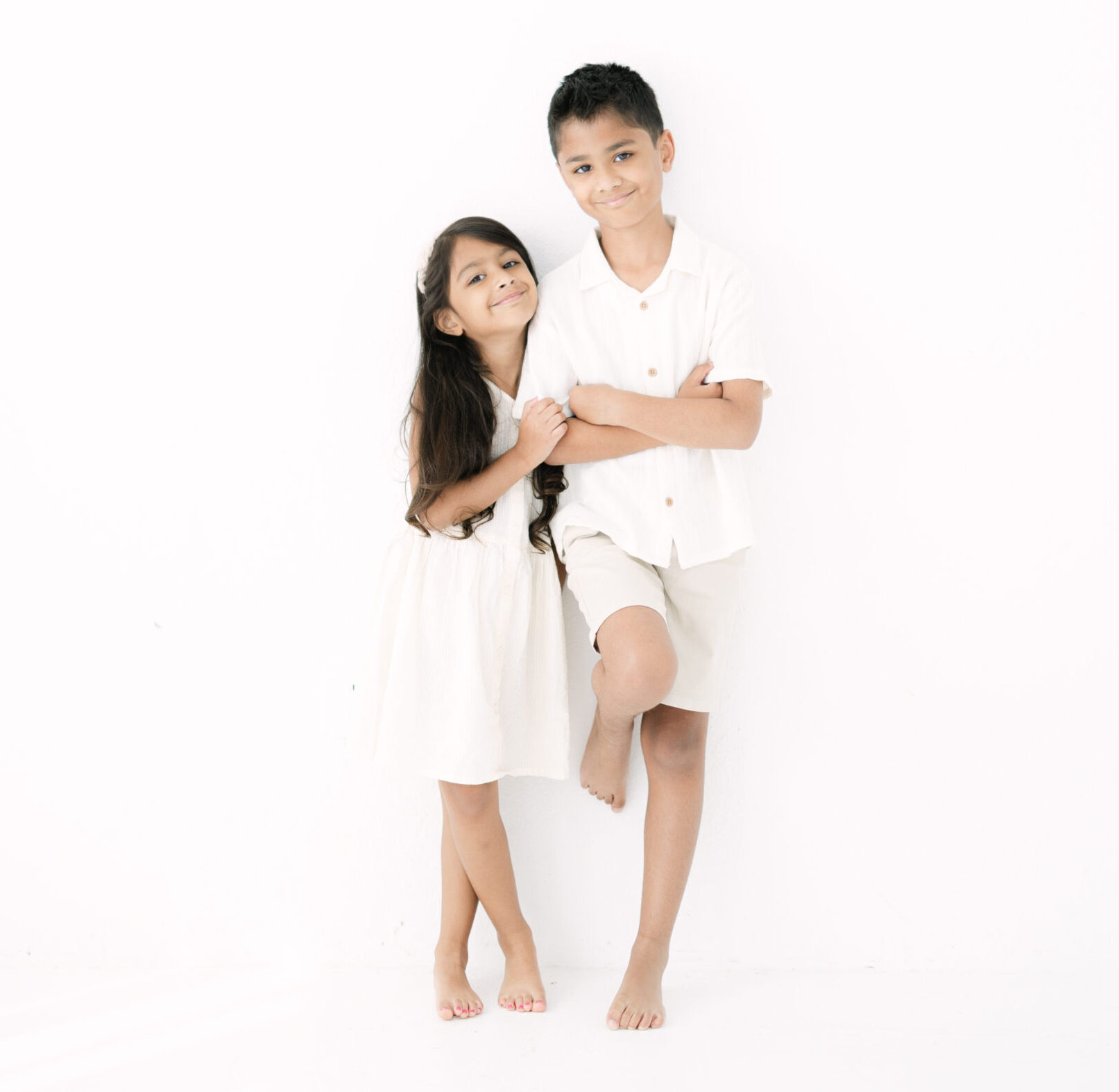 Two children in white standing together in a studio portrait